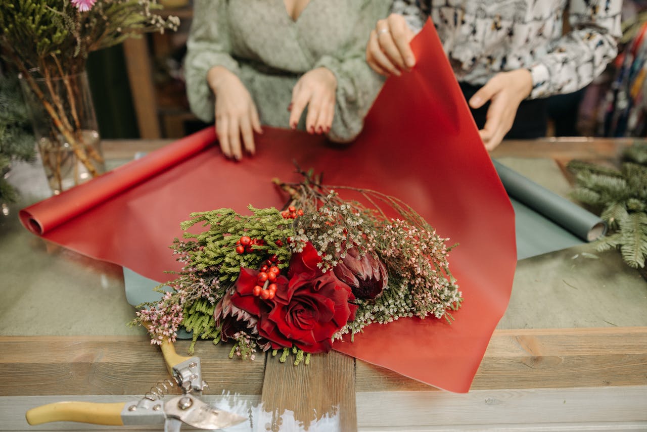 Florists wrapping a vibrant flower bouquet with red roses and greenery on red paper.